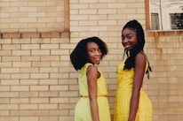 two women wearing yellow sleeveless dresses near brown brick