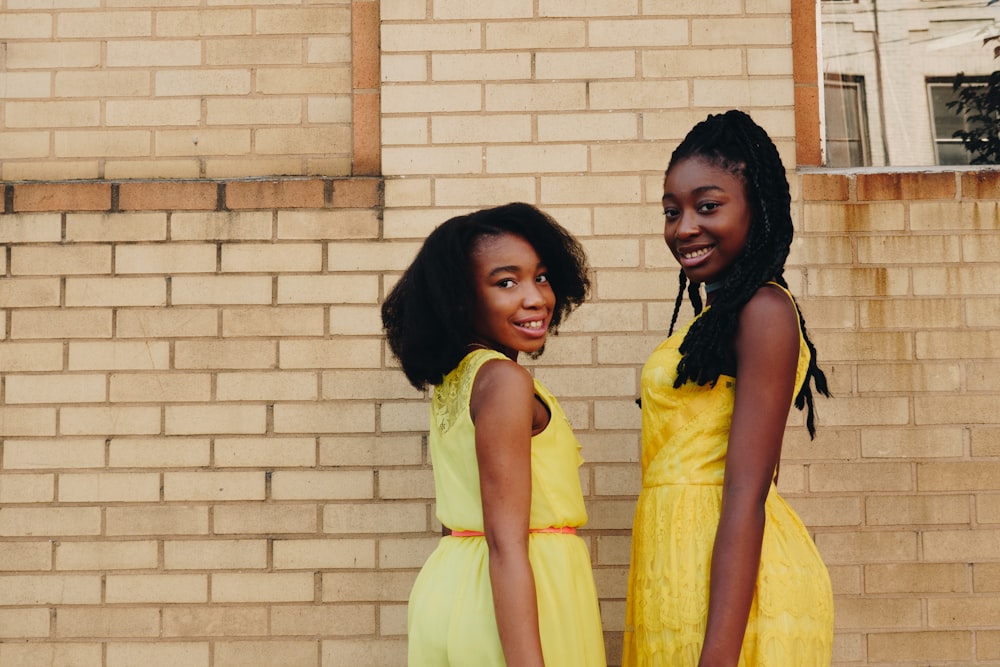 two women wearing yellow sleeveless dresses near brown brick