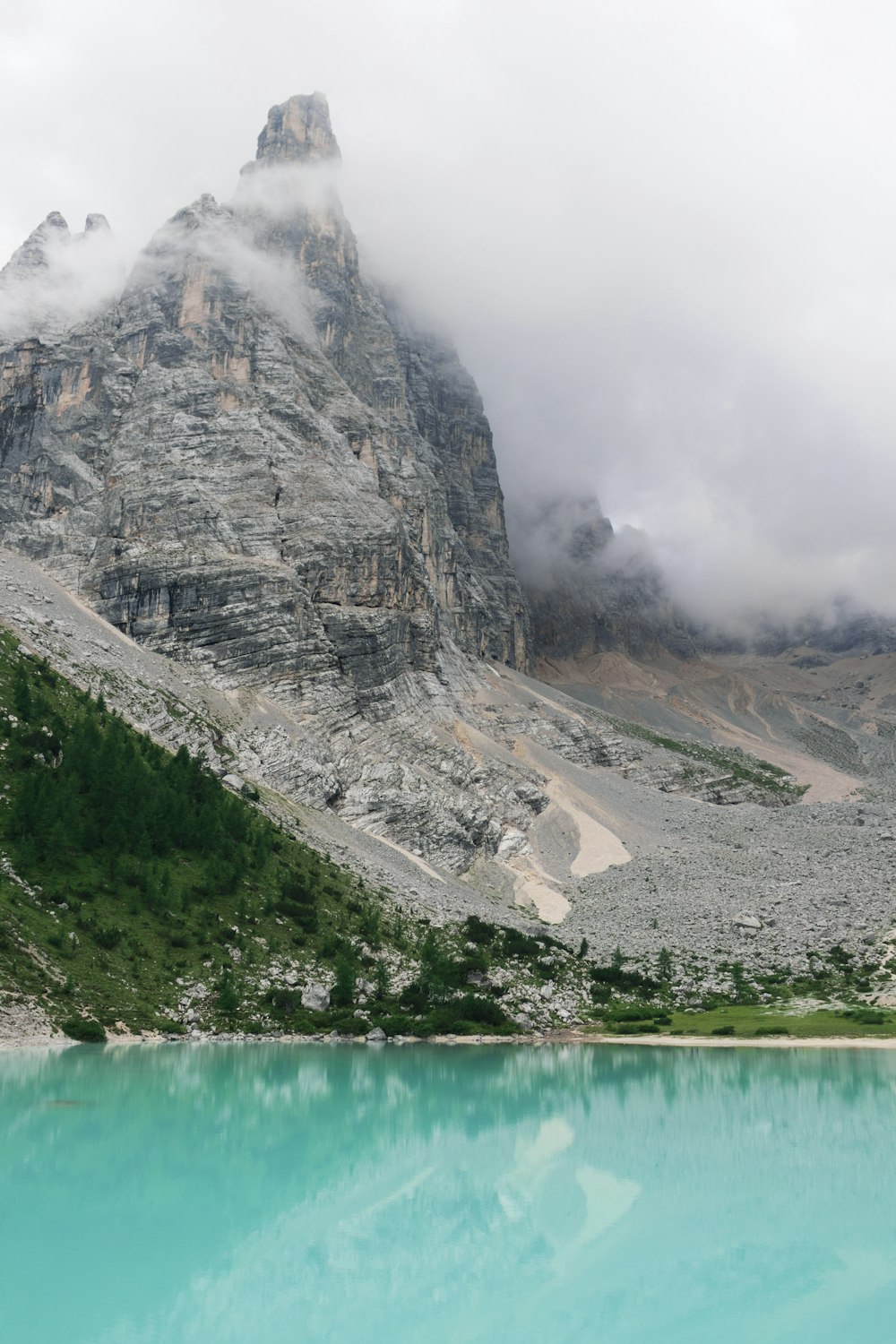 specchio d'acqua ai piedi della montagna circondato da nuvole