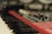 A close-up of a red synthesizer with black and white piano keys visible in the foreground. Several knobs and buttons are present on the synthesizer's control panel with a soft focus effect creating a blurred background.