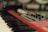 A close-up of a red synthesizer with black and white piano keys visible in the foreground. Several knobs and buttons are present on the synthesizer's control panel with a soft focus effect creating a blurred background.