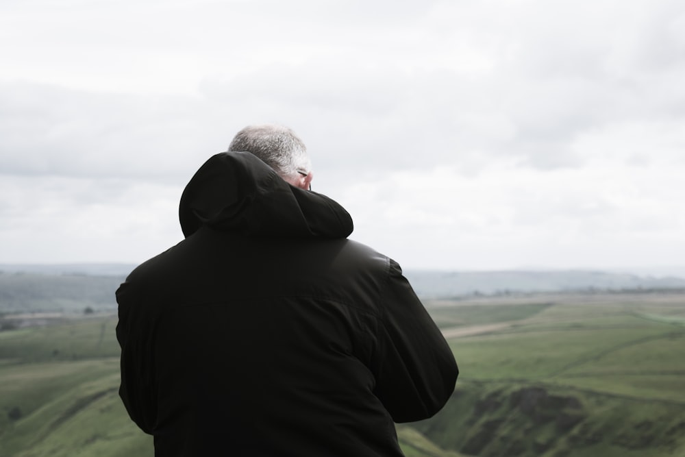 man wears black hooded jacket on green grass