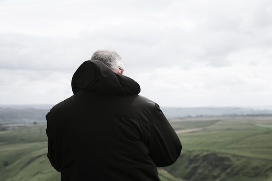 man wears black hooded jacket on green grass in Mam Tor United Kingdom