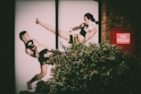 A photograph of a mural or poster depicting two martial artists in mid-action, covered partially by greenery. The male figure appears to deflect a high kick from the female figure. A red fire hydrant box is visible on a brick wall beside the mural.