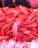 A pile of freshly caught prawns is displayed on a bed of ice. The prawns have a vibrant pinkish-red color, and their shiny, wet shells are clearly visible. The ice beneath them is crushed and white, contrasting with their bold color. Some of the prawns have long antennae visible.