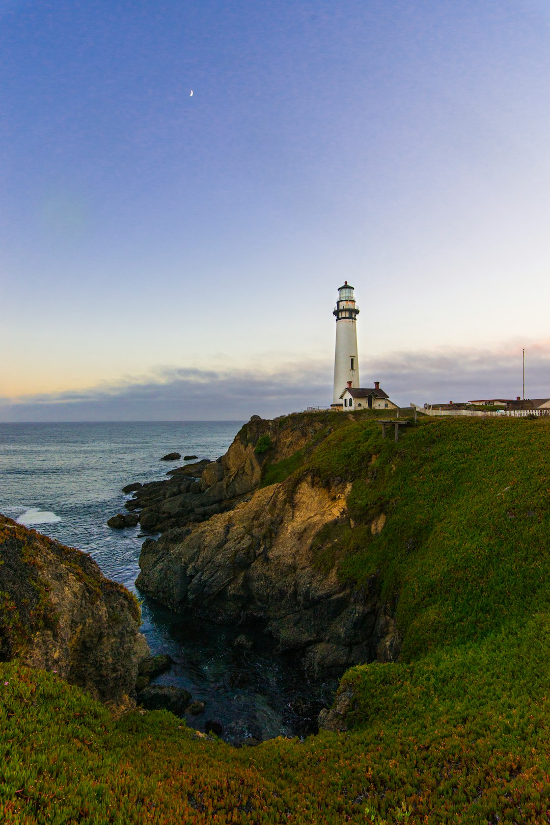 white lighthouse on green grass field near body of water during daytime