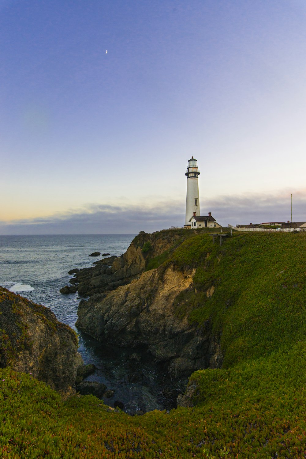 white lighthouse on green grass field near body of water during daytime