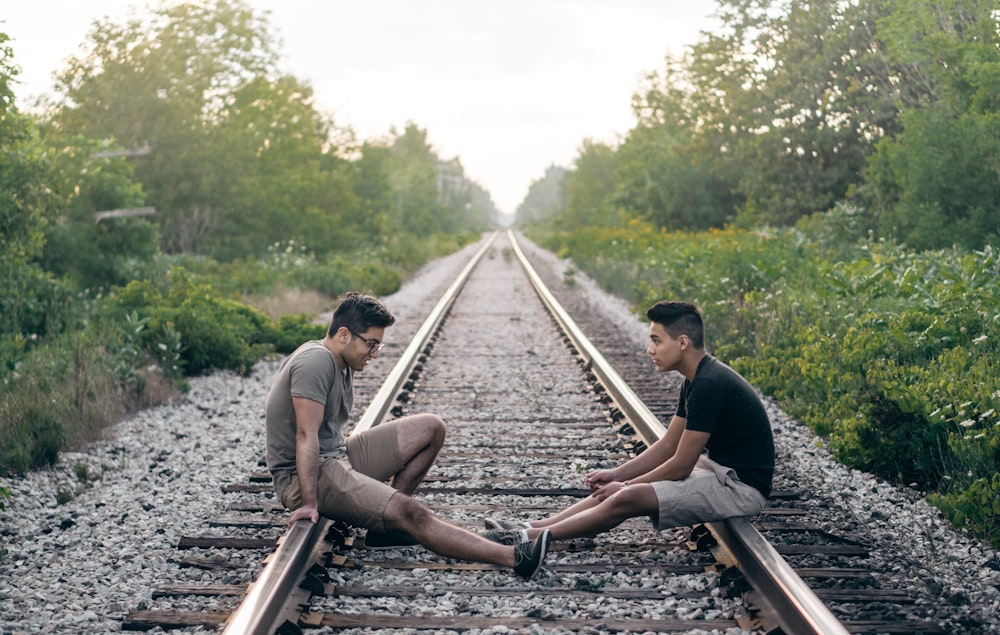 2 person sitting on train rails during daytime