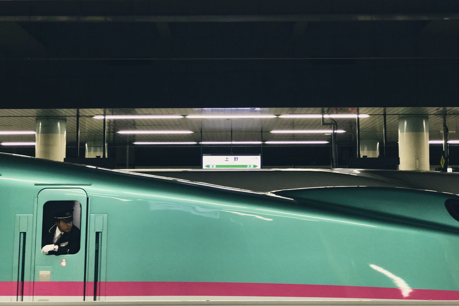 A train conductor checks the platform from the window of a green train in Japan.