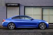 blue coupe beside gray house