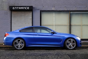 blue coupe beside gray house