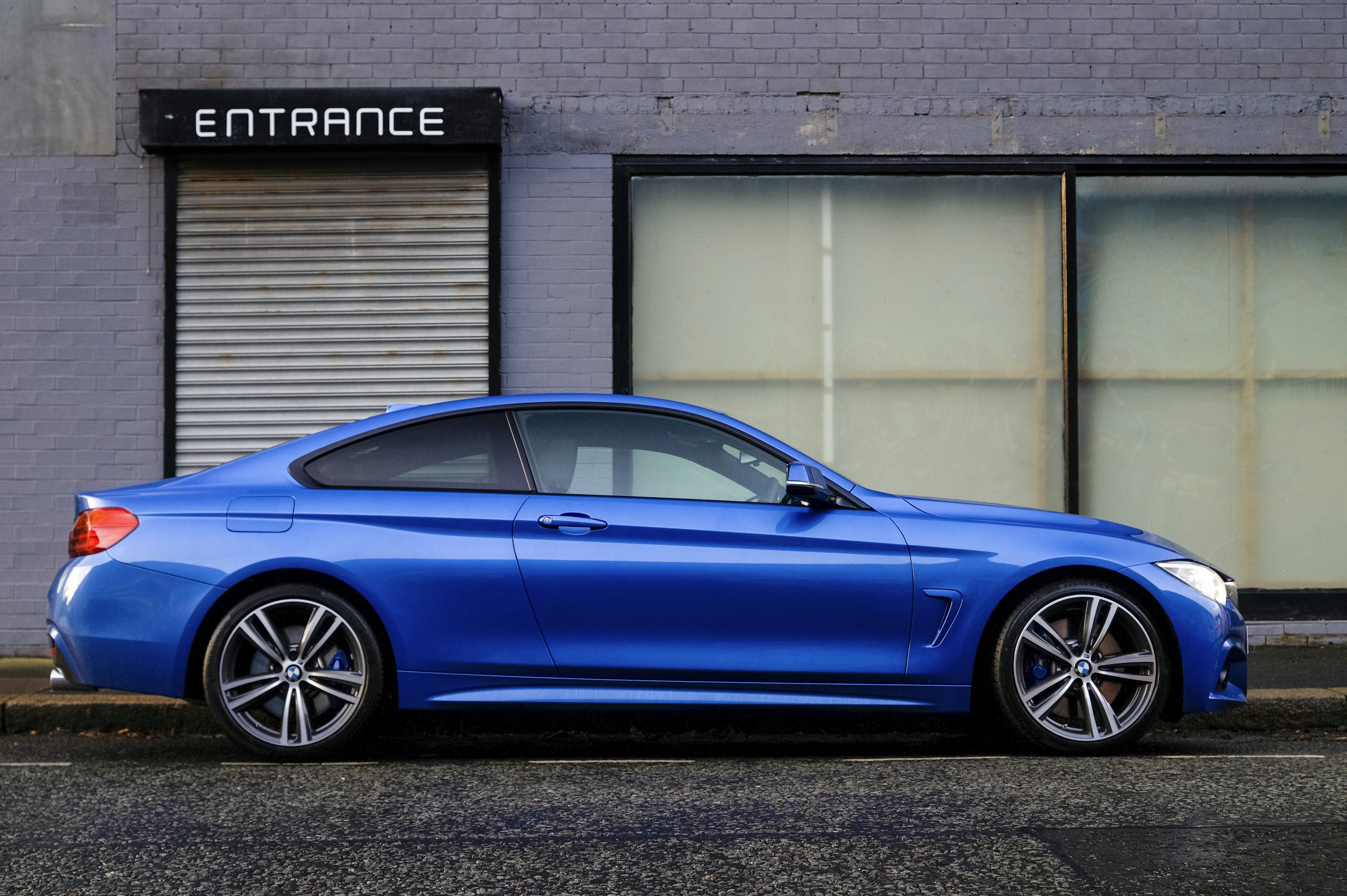 blue coupe beside gray house