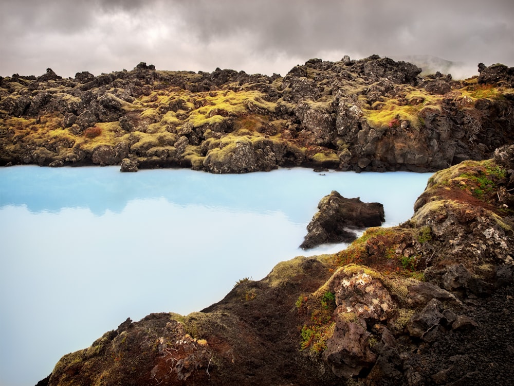 Cuerpo de agua entre rocas bajo cielo nublado durante el día