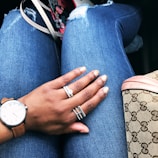 Close-up of a hand adorned with layered rings and a chic watch, resting on a textured leather handbag.