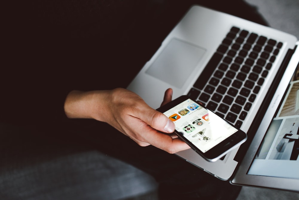 person holding smartphone and laptop