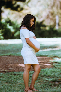 A pregnant woman gently holding her belly while practicing prenatal yoga outdoors.