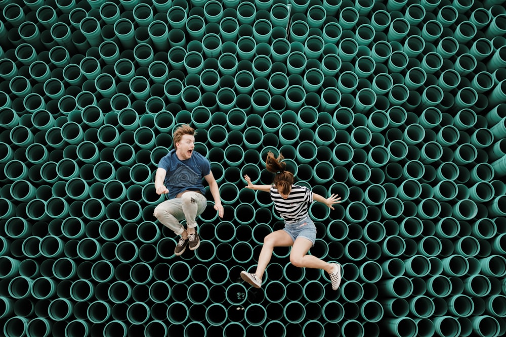 minimalist photography of man and woman jumping in front of tube wall