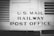 The image features a vintage railway car with the words 'U.S. Mail Railway Post Office' prominently displayed. The surface is metallic and riveted, suggesting an industrial design from the early to mid-20th century. The image is in black and white, enhancing its historical feel.