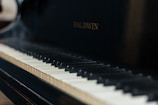 A close-up view of a piano keyboard with the brand name Baldwin visible on the piano body. The keys have a mix of black and white keys with visible shadows.