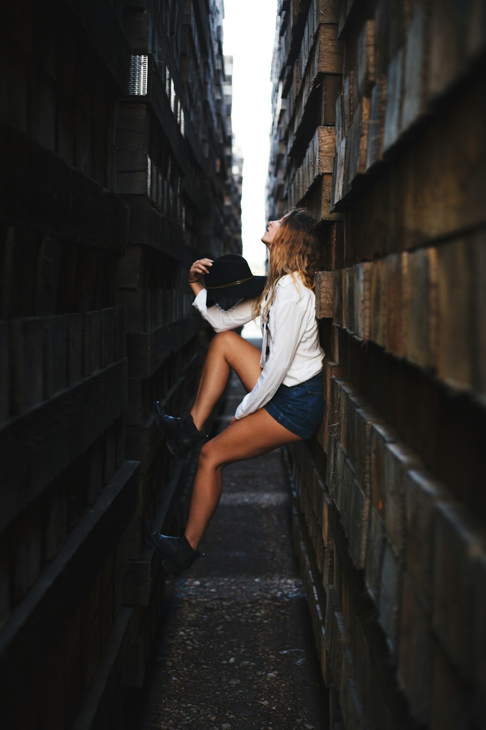 woman holding her hat leaning on brick wall