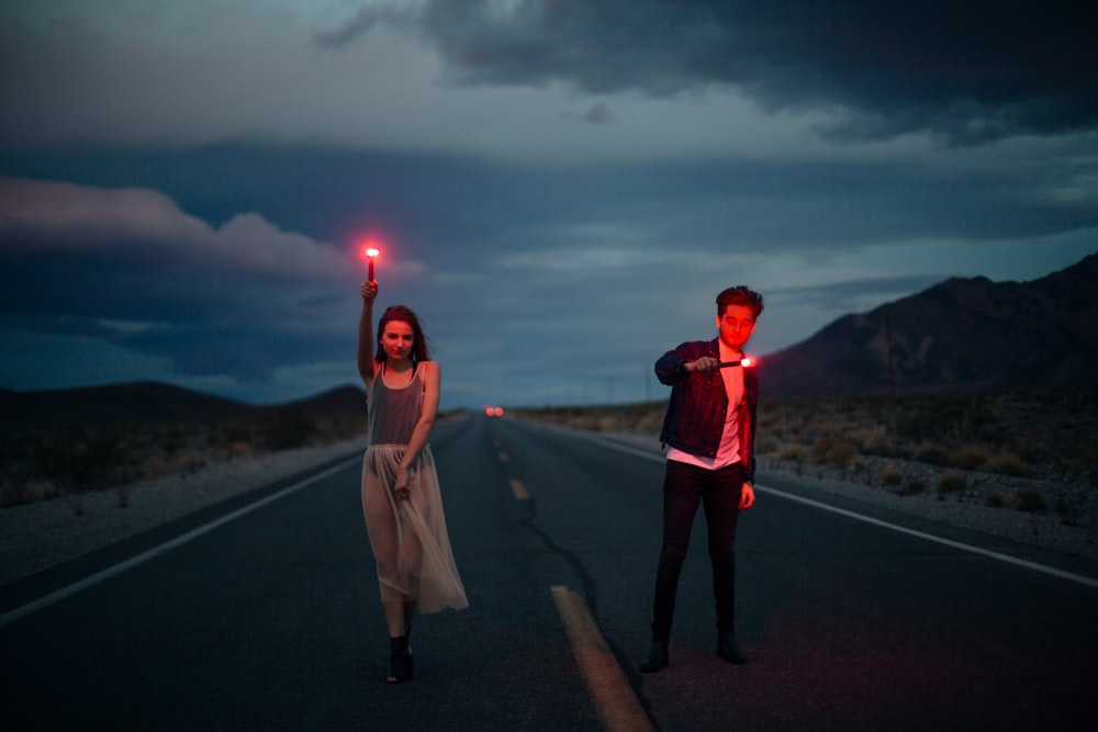 man and woman holding red flare on yellow line road