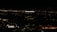 A tall building with the illuminated sign of a well-known media company stands against a backdrop of a cityscape at night. Numerous small lights are scattered across the landscape, indicating urban activity in the distance.