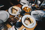 White disposable plates stacked with a variety of finger foods on a wooden table