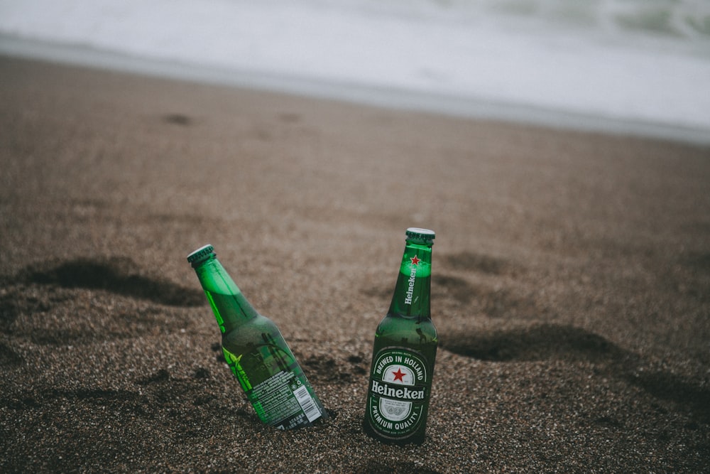 two green Heineken bottles on gray soil