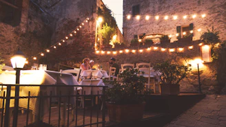 A cozy outdoor dining setup with a crisp white tablecloth, surrounded by greenery and soft string lights.