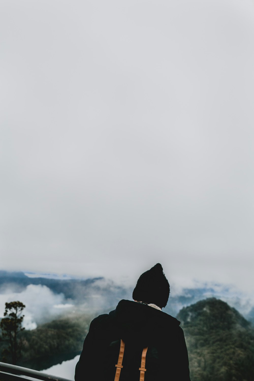 Mann mit schwarzer Jacke und Strickmütze mit Blick auf grüne Berge