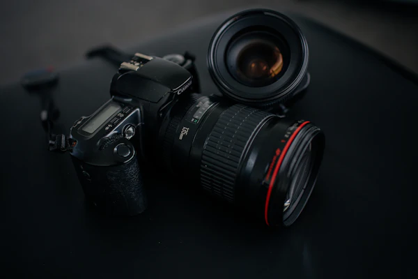 Koyu bir zemin üzerinde duran siyah DSLR fotoğraf makinesi ve yanında kırmızı halkalı bir lens