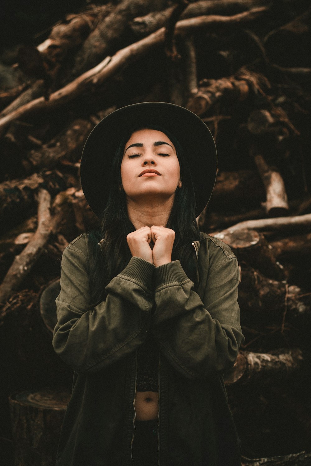 woman closing her eyes near pile of logs