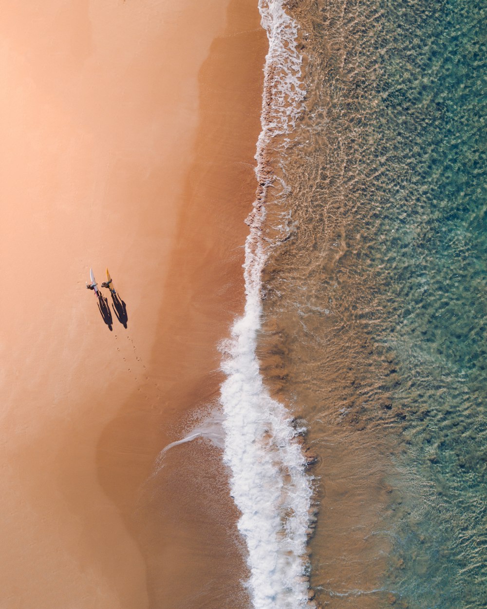 aerial photography of two persons walking along seashore during daytime