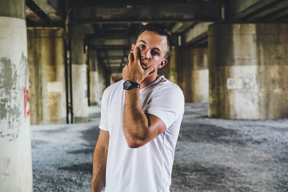 man in white crew-neck t-shirt standing near gray concrete pillar