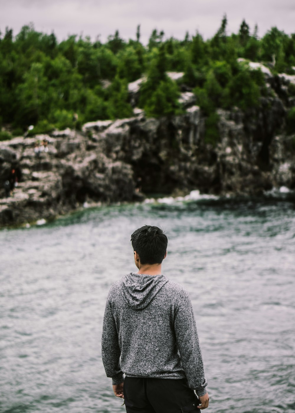 man facing backward fronting body of water and trees foliage