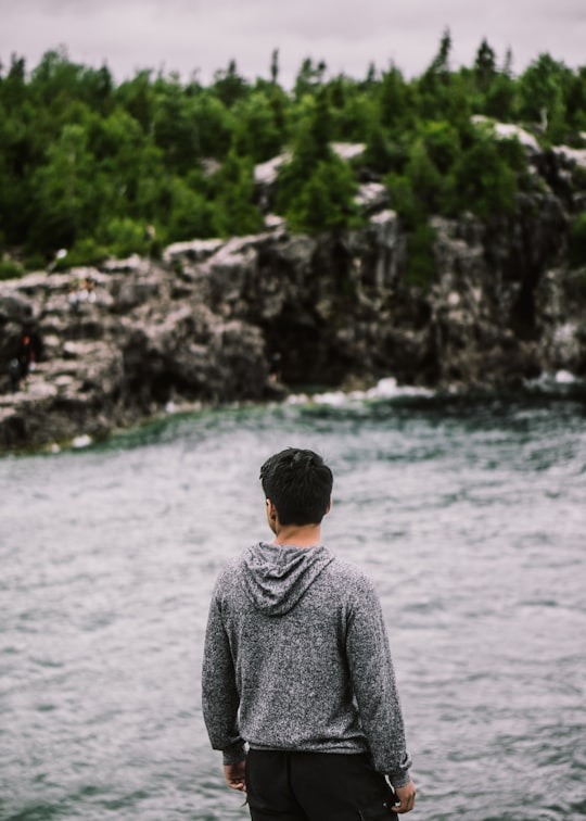 man facing backward fronting body of water and trees foliage in Tobermory Canada