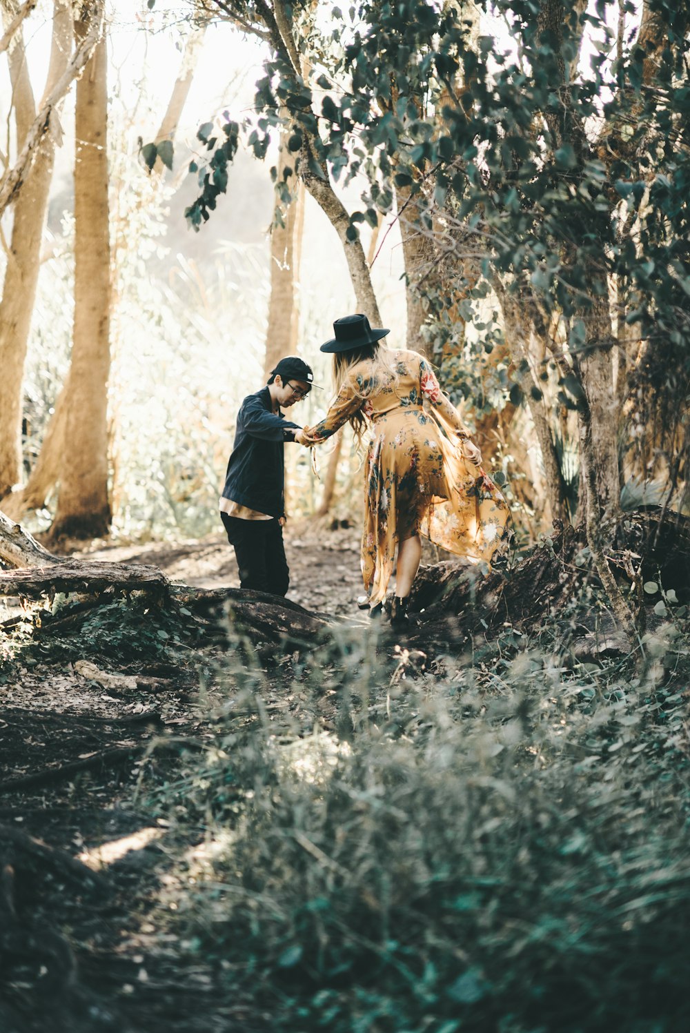 man helping woman cross tree trunk