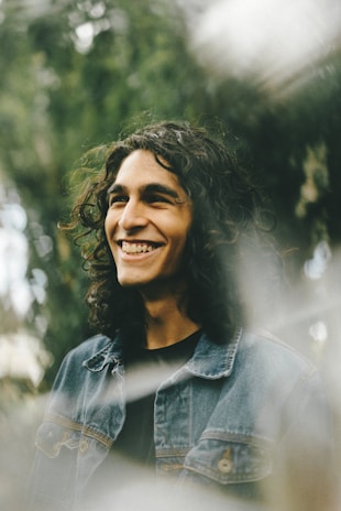 A smiling customer outdoors, wearing a denim jacket from airden, with city buildings blurred in the background.