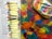 A collection of acrylic paint tubes is arranged on a newspaper. Beside them lies a colorful palette covered with various shades of paint, and several paintbrushes rest on top. The colors are vibrant and diverse, with an abstract background of mixed hues.