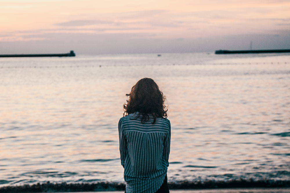 woman in front ocean water under white sky