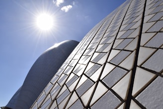 Sunlight shines brightly over the geometric tiled surface of a modern architectural structure, creating patterns of light and shadow.