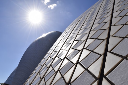 Sunlight shines brightly over the geometric tiled surface of a modern architectural structure, creating patterns of light and shadow.