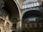 The image captures an elegant architectural interior featuring large, arched windows with intricate metal and stone detailing. The walls are adorned with decorative elements and columns, showcasing a blend of classical and industrial styles.