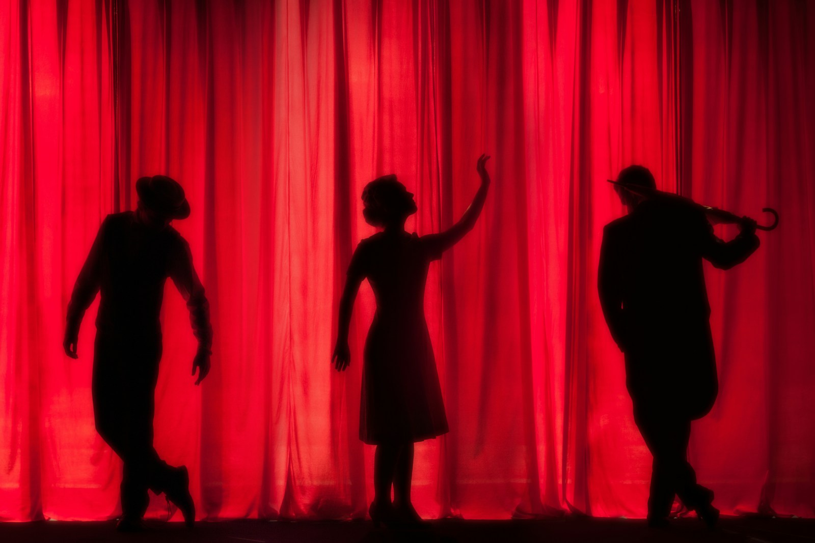 silhouettes of actors in front of a red curtain