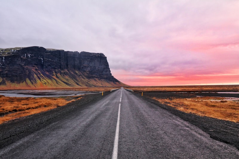 Empty two-lane road running toward a sheer cliff on the horizon under an overcast Icelandic sky