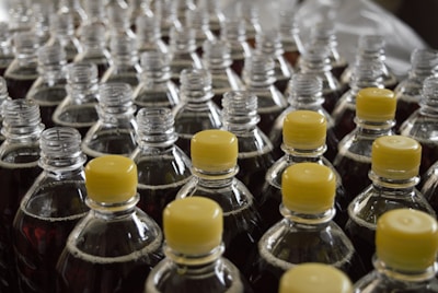 Rows of plastic bottles, each topped with a yellow cap, filled with a dark liquid. The bottles are arranged closely together, creating a sense of repetition and uniformity.