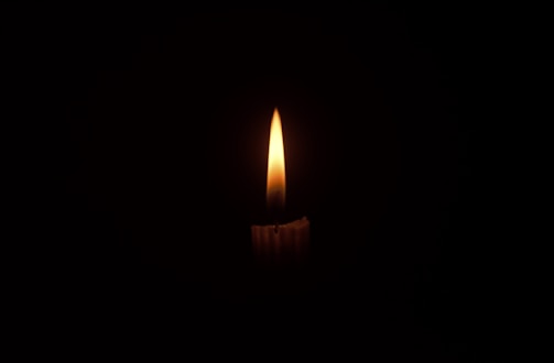 A serene candle flame flickering gently in a dark room, symbolizing remembrance and peace.