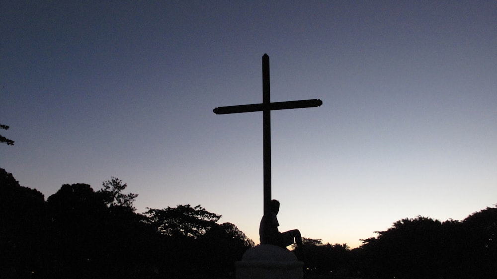 Silhouette einer Person, die unter dem Kreuz sitzt