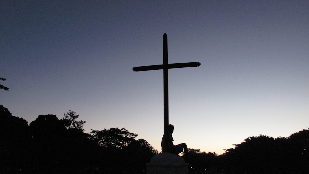 silhouette of person sitting below cross