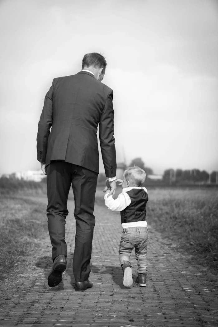 Pai de terno caminhando de mãos dadas com o filho pequeno